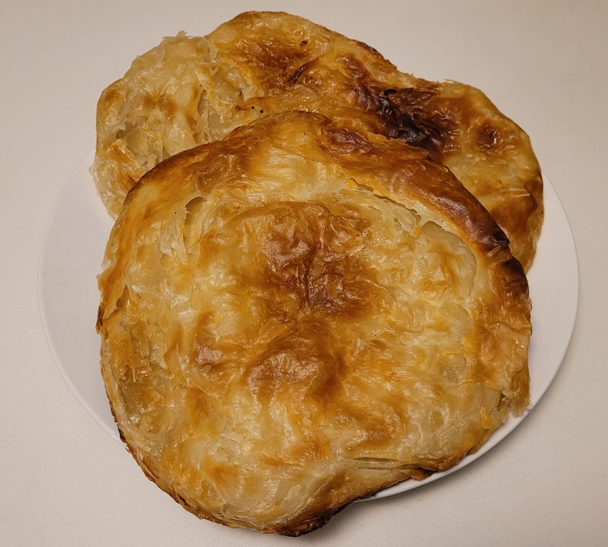 Golden Egyptian Feteer Meshaltet — golden round Egyptian flaky layered pastry on a white plate